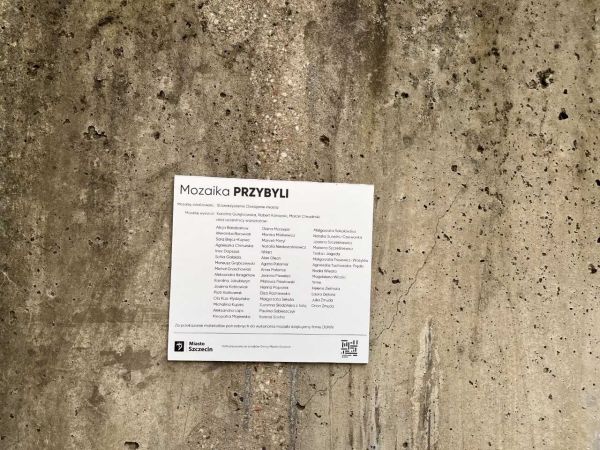 Tablica z nazwiskami twórców na tle muru