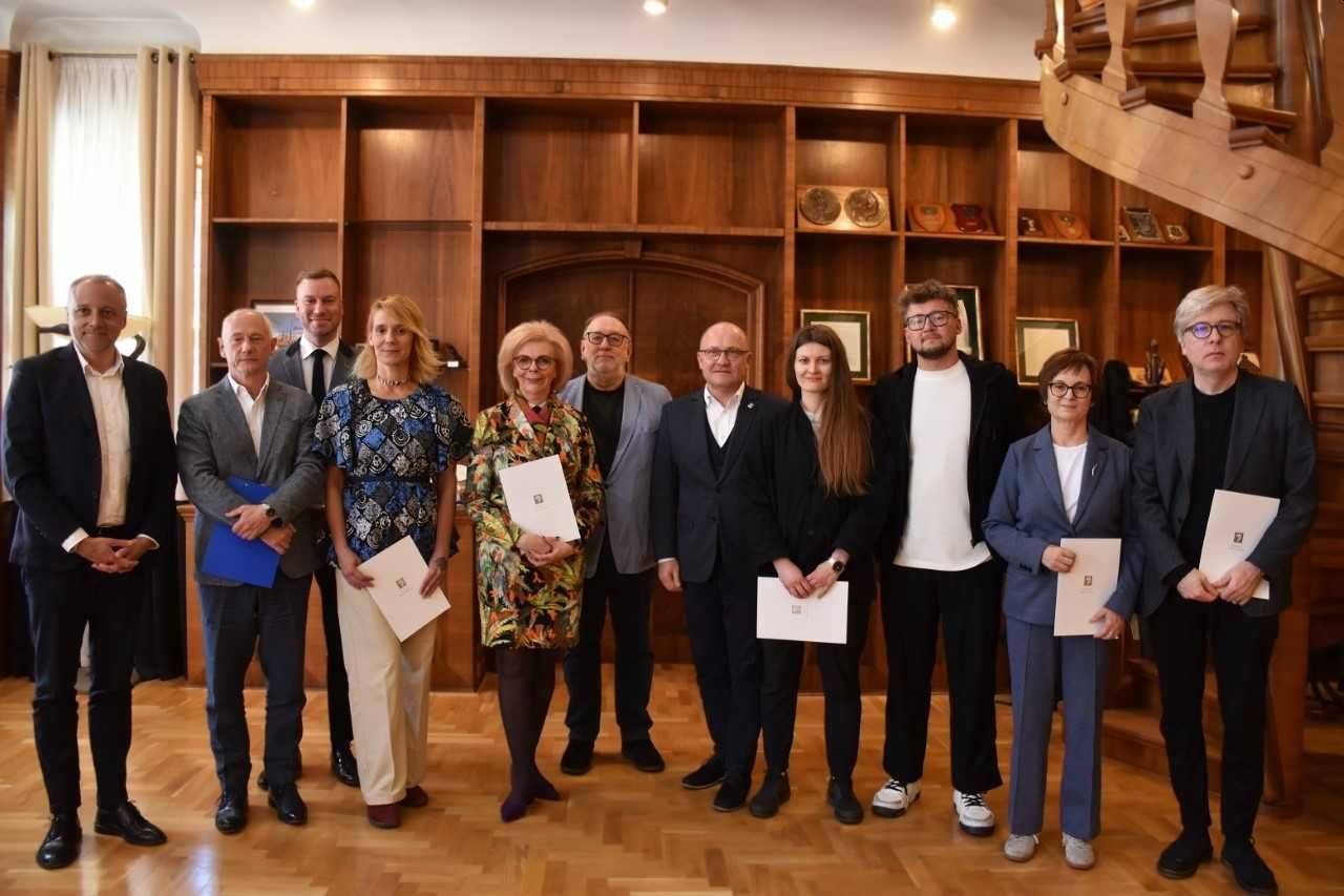 Grupa jedenastu osób, w tym cztery kobiety, stoi na tle regału z medalami